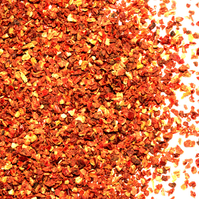 Close-up of Whole Spice Inc. Tomato Flakes spread on a white surface, displaying vibrant red and orange hues and appealing textures.