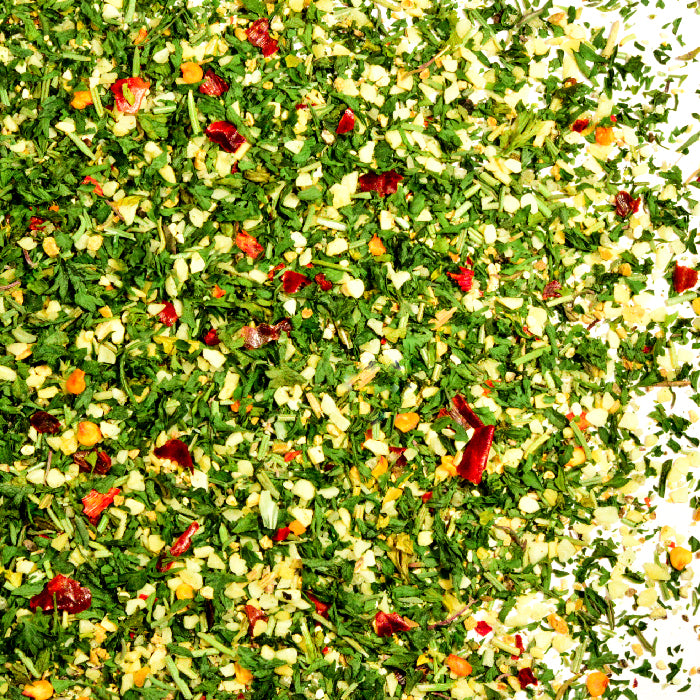 A close-up of Whole Spice Inc. Venison Roast Seasoning shows a vibrant blend with chopped green herbs, red chili flakes, and yellow bits—perfect for seasoning venison roast or adding rich flavor to stews.