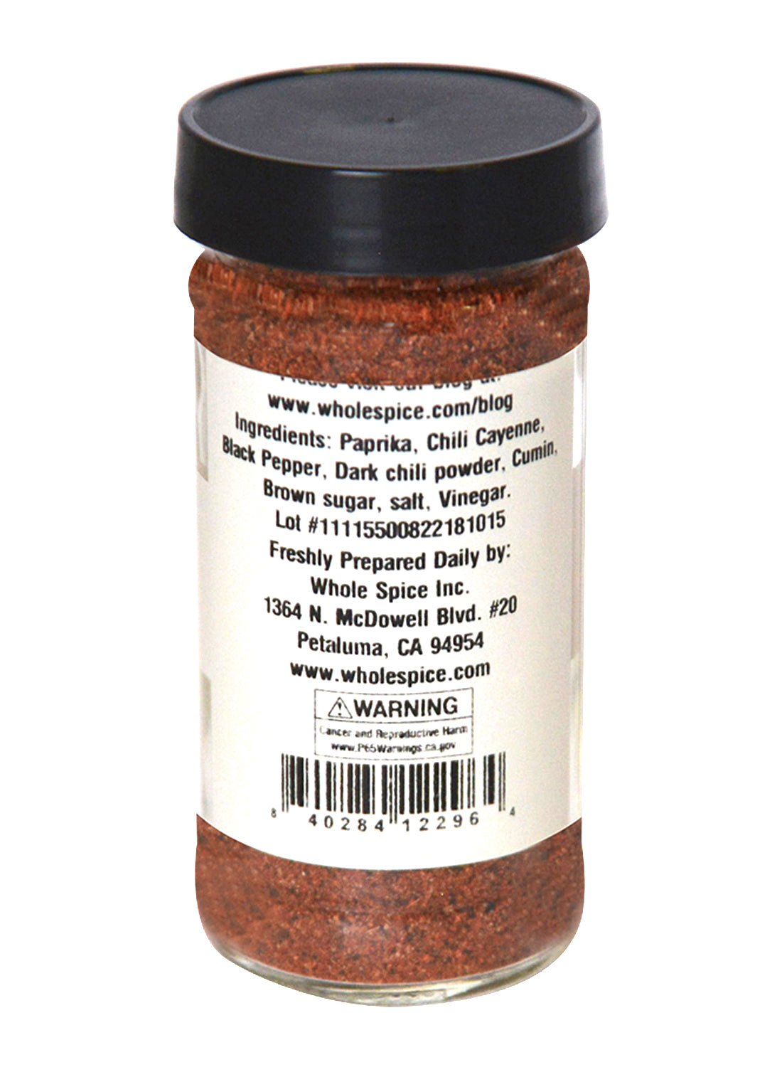 A clear spice jar with a black lid holds Whole Spice Inc.’s Vinegar BBQ Rub, a reddish-brown mix of paprika, chili, black pepper, cumin, brown sugar, and apple cider vinegar. The label includes company info and a barcode.