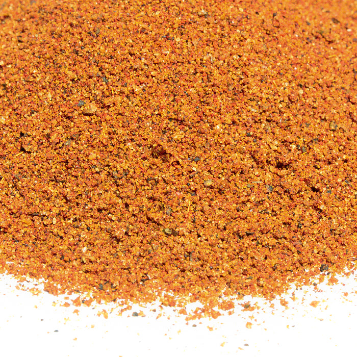 A close-up of Whole Spice Inc. Vinegar BBQ Rub, a finely ground, reddish-orange seasoning inspired by classic Carolina Barbeque, on a white surface.