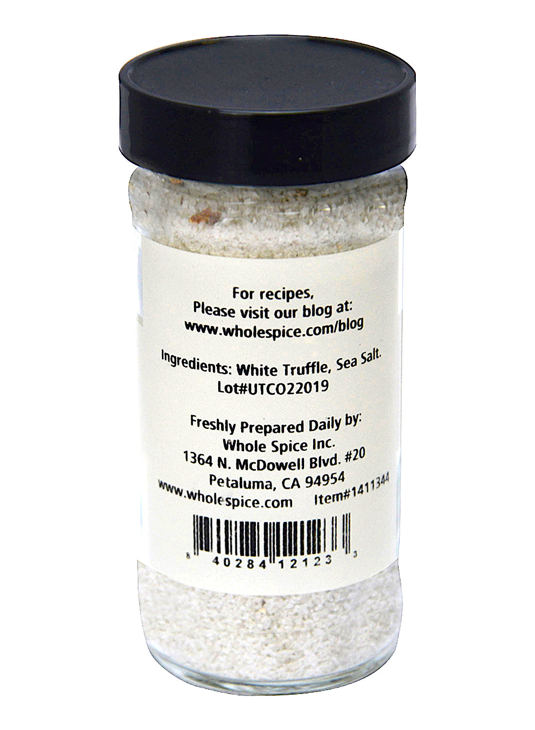 A clear glass jar with a black lid holds White Truffle Sea Salt by Whole Spice Inc. The label lists ingredients, company address (Petaluma, CA), and invites you to visit the company blog for recipes.