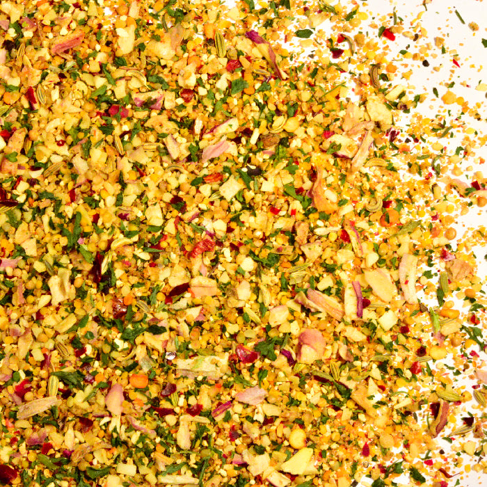 A close-up of Whole Spice Inc. Wild Game Seasoning, a vibrant blend of dried herbs, garlic, onion, and spices, scattered on a white background.