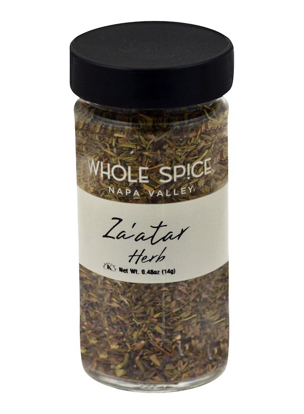 A clear glass jar with black lid contains Za'atar Herb by Whole Spice Inc. The label shows "Za’atar Herb" and net weight 0.48 oz (14g); the classic Middle Eastern blend is visible inside.