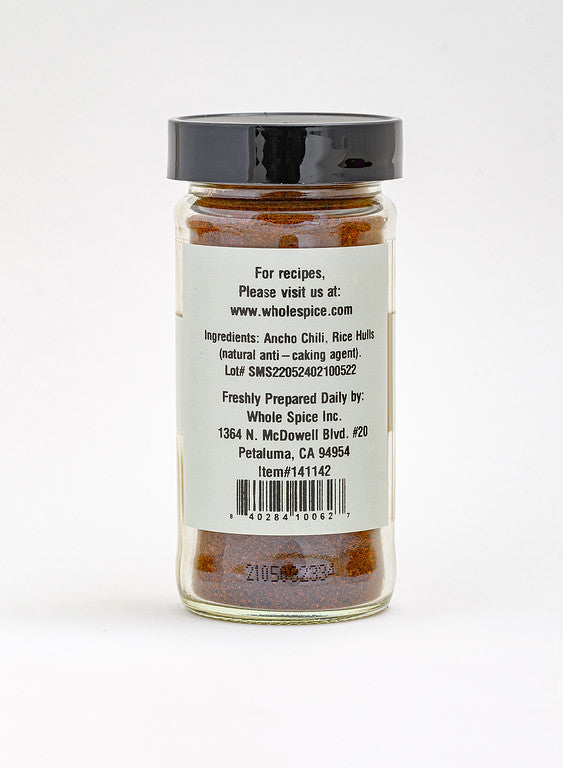 A glass jar labeled "Ancho Chili Powder" from Whole Spice Inc. is shown from the back, listing ingredients as ancho chili and rice hulls—ideal for adding rich flavor to Mexican dishes like mole—with contact info for Whole Spice in Petaluma, CA.
