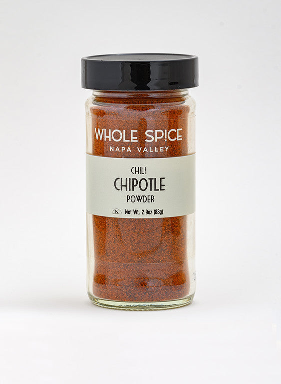 A glass jar of Whole Spice Inc. Chipotle Chili Powder features a black lid and white label displaying the product name and 2.9 oz (83g) net weight, perfect for adding smoky heat to dishes, shown against a plain white background.