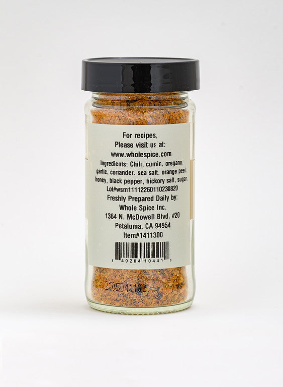 A clear spice jar with a black lid displays Whole Spice Inc.'s Chipotle Honey Rub, a coarse barbecue blend featuring chili, cumin, coriander, and hickory smoked sea salt. The label includes company info from Petaluma, CA.