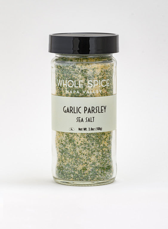 A clear glass jar with a black lid contains Whole Spice Inc. Garlic & Parsley Sea Salt, featuring a green and white coarse mix visible through the cream label—ideal for sprinkling or as a dip seasoning.
