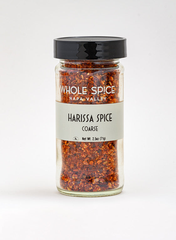 A 2.5 oz (71g) glass jar of Whole Spice Inc. Harissa Spice Coarse, with a black lid and gray label, features a crushed red chili blend for flavorful, spicy seasoning.