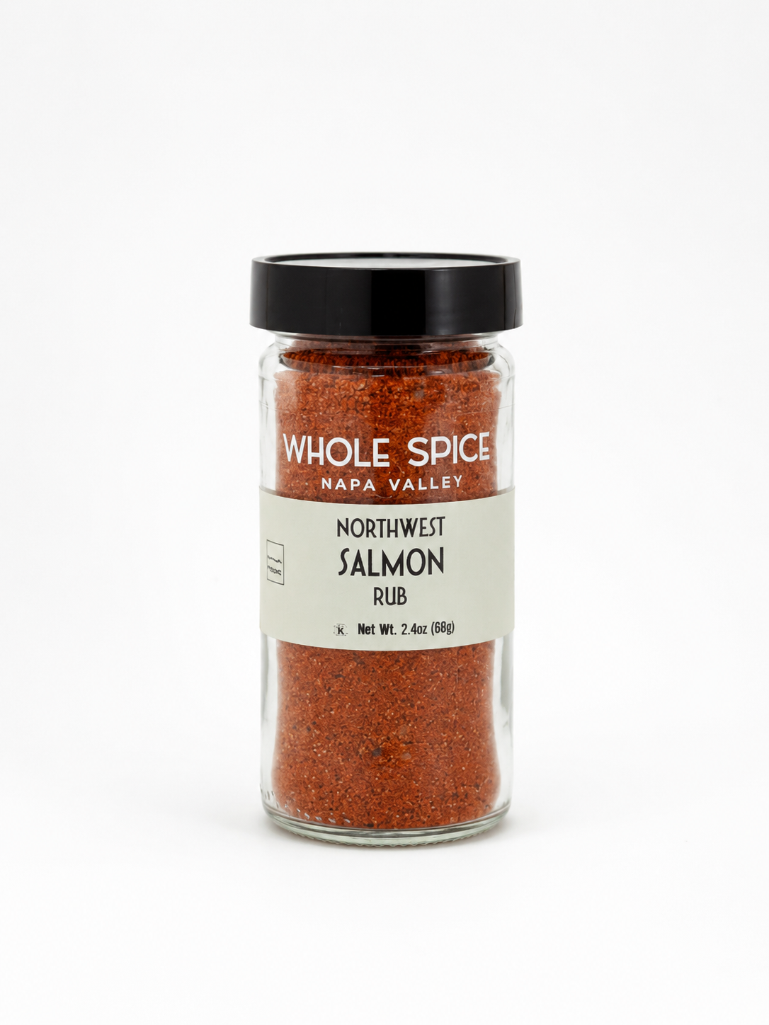 A glass jar of Whole Spice Inc. Northwest Salmon Rub, topped with a black lid and brimming with a reddish gourmet blend, is displayed on a white background—ideal for enhancing your cedar plank salmon dishes.