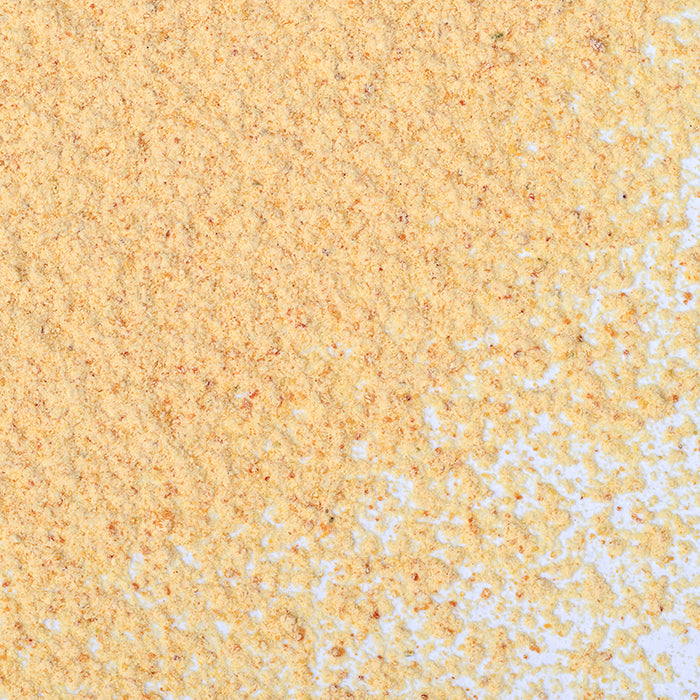 A close-up of Whole Spice Inc. Onion Toasted Powder scattered on a white surface, with a dense patch in the top left that gradually thins toward the bottom right.