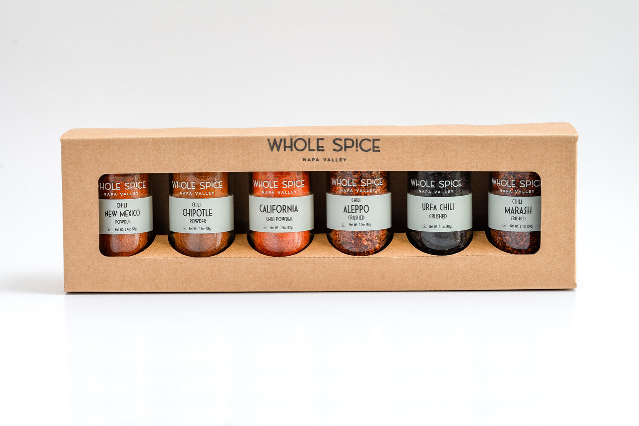 The Whole Spice Chili Gift Set by Whole Spice Inc. features six glass jars—New Mexico, Chipotle, California, Aleppo, Urfa Chili, and Marash—in a light brown box with a clear front panel.