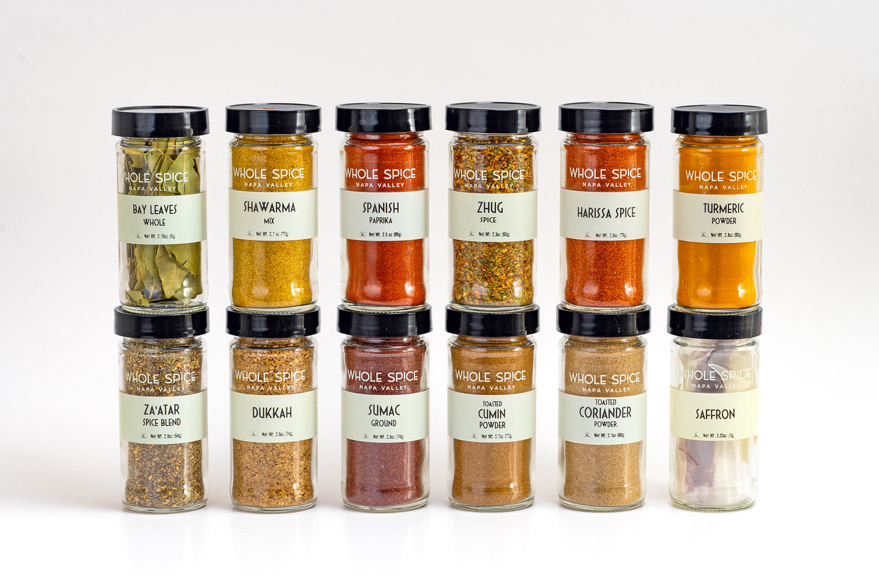 The Whole Spice Middle Eastern Jar Set by Whole Spice Inc. features 12 jars in two rows on a white background, each labeled with spices like za’atar, sumac, harissa spice, dukkah, bay leaves, shawarma blend, zhug seasoning, and more.