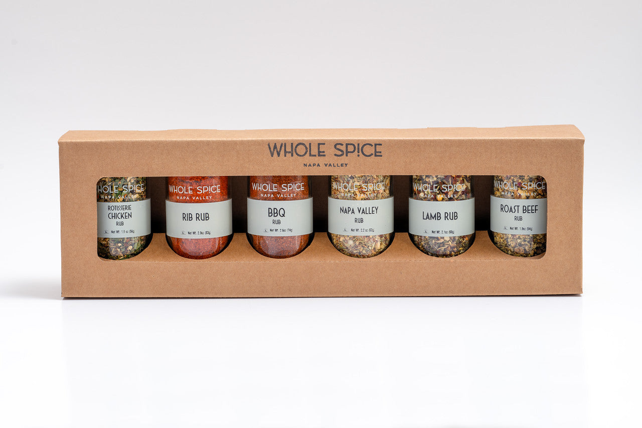 A Whole Spice Inc. Spice Rubs Gift Set features a cardboard box with six seasoning jars—Rotisserie Chicken, Rib Rub, BBQ Rub, Napa Valley, Lamb Rub, and Roast Beef—arranged side by side.