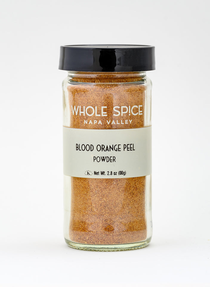 A clear glass jar with a black lid labeled Whole Spice Inc. Blood Orange Peel Powder, Net Wt. 2.8 oz (80g), ideal for baking, is displayed on a light background.