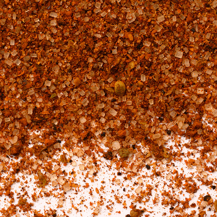 A close-up of Whole Spice Inc.'s Coffee Rub shows coarse salt crystals, reddish-brown seasoning, and small herb pieces scattered on a white background.