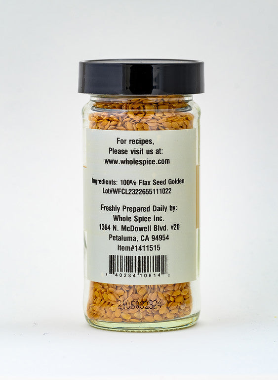 A clear glass jar with a black lid holds Flax Seeds Golden by Whole Spice Inc. The label lists the ingredient as 100% flax seed golden, with contact and location details for Whole Spice Inc. on the back.