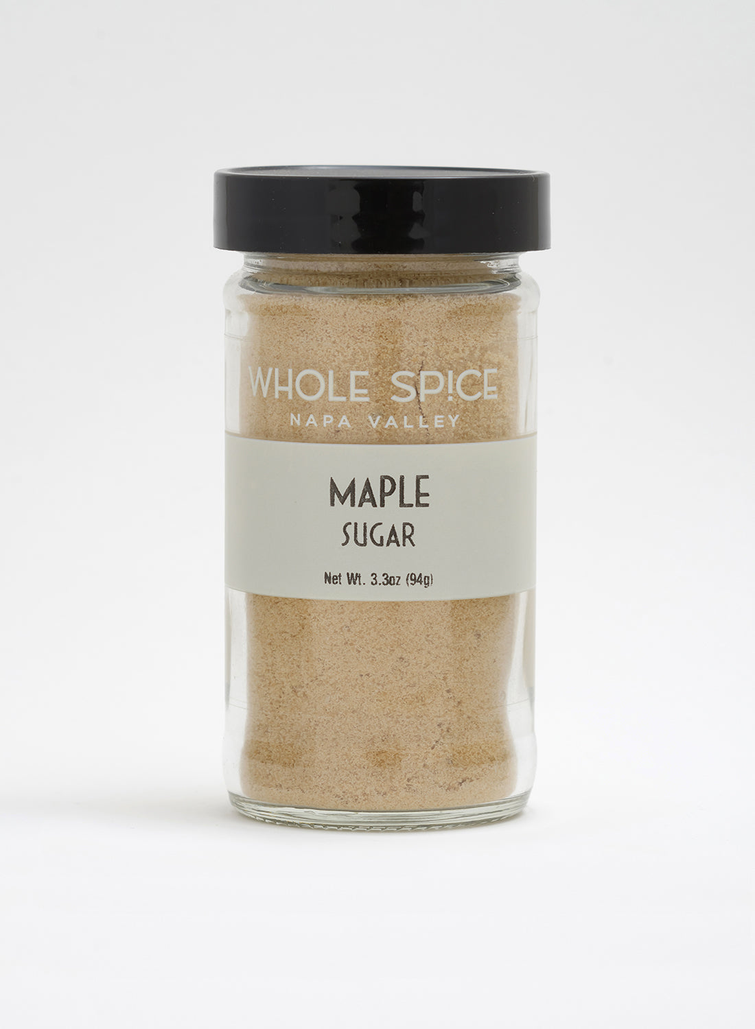 A clear glass jar with a black lid, labeled “Whole Spice Inc. Maple Sugar,” contains 3.3 oz (94g) of light brown maple sugar granules made from pure maple syrup—a natural sweetener.