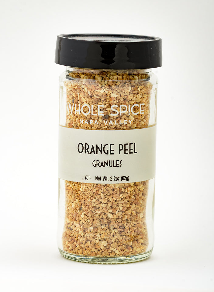 A clear glass jar with a black lid labeled Whole Spice Inc. Orange Peel Granules, Net Wt. 2.2oz (62g), contains dried orange zest to add vibrant citrus flavor to your dishes, set against a plain white background.
