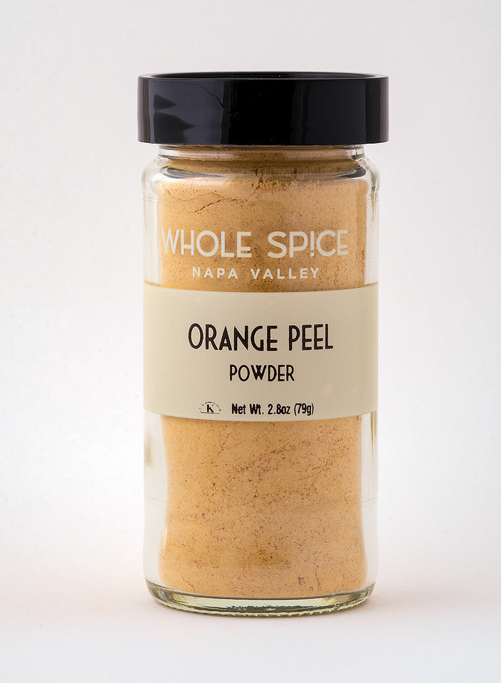 A glass jar with a black lid, labeled Whole Spice Inc. Orange Peel Powder, contains 2.8 oz (79g) of vibrant citrus-flavored powder. The jar is photographed against a plain white background.
