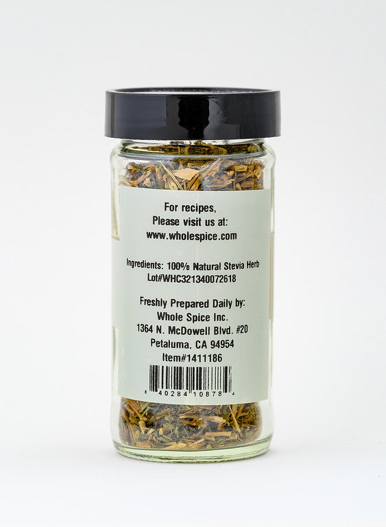 A clear glass jar with a black lid contains Stevia Leaf from Whole Spice Inc. The label lists ingredients, company address, item number, and website. The jar stands upright on a white background.