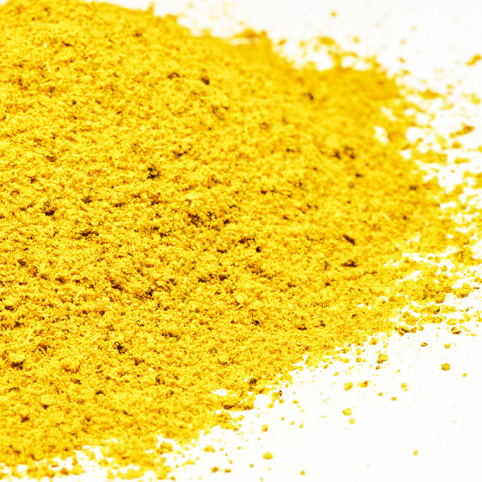 A close-up of Afghan Ribs Blend by Whole Spice Inc., a vibrant yellow poultry spice mix often used in grilling, scattered on a white surface.