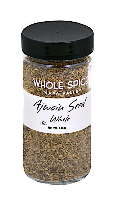 A clear glass jar with a black lid contains Ajwain Seed Whole by Whole Spice Inc., an essential Indian spice, Net Wt. 1.8 oz.