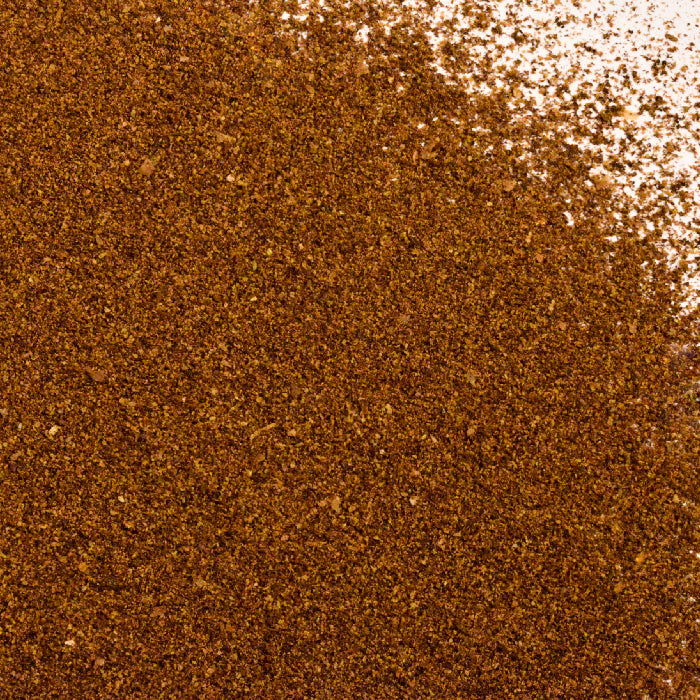 Close-up of Whole Spice Inc. Allspice Powder, showing a dense pile of finely ground spice covering most of the white background, with a lighter dusting in the top right corner.