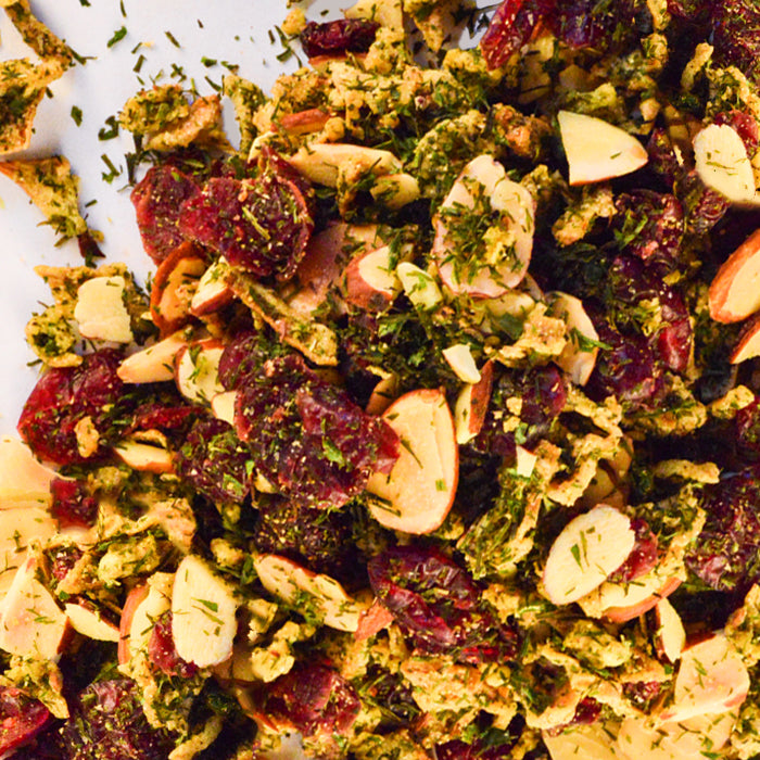 A close-up of a salad with sliced almonds, dried cranberries, shredded greens, and herbs, all tossed with Whole Spice Inc. Almond Cranberry Rice Seasoning on a light surface.