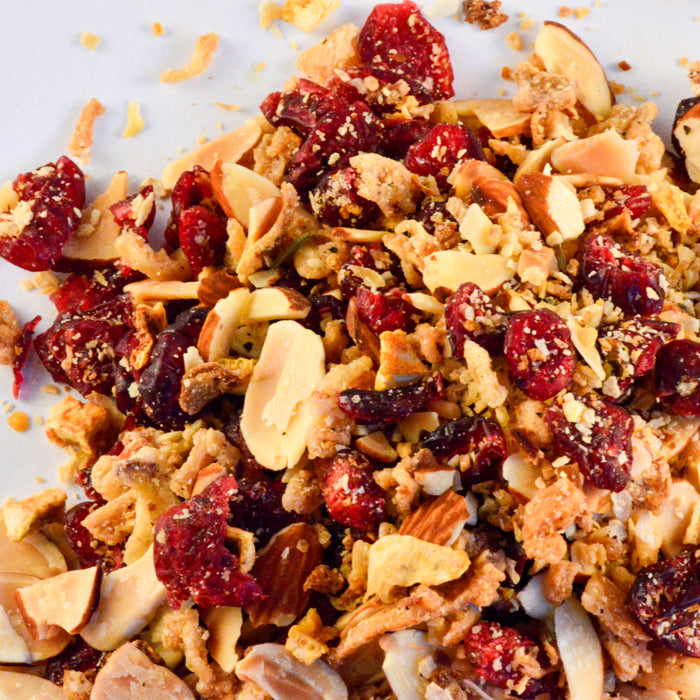 A close-up of granola with dried cranberries, sliced almonds, and crunchy clusters on a white surface evokes the vibrant flavors of Whole Spice Inc. Almond Cranberry Orange Rice Seasoning.