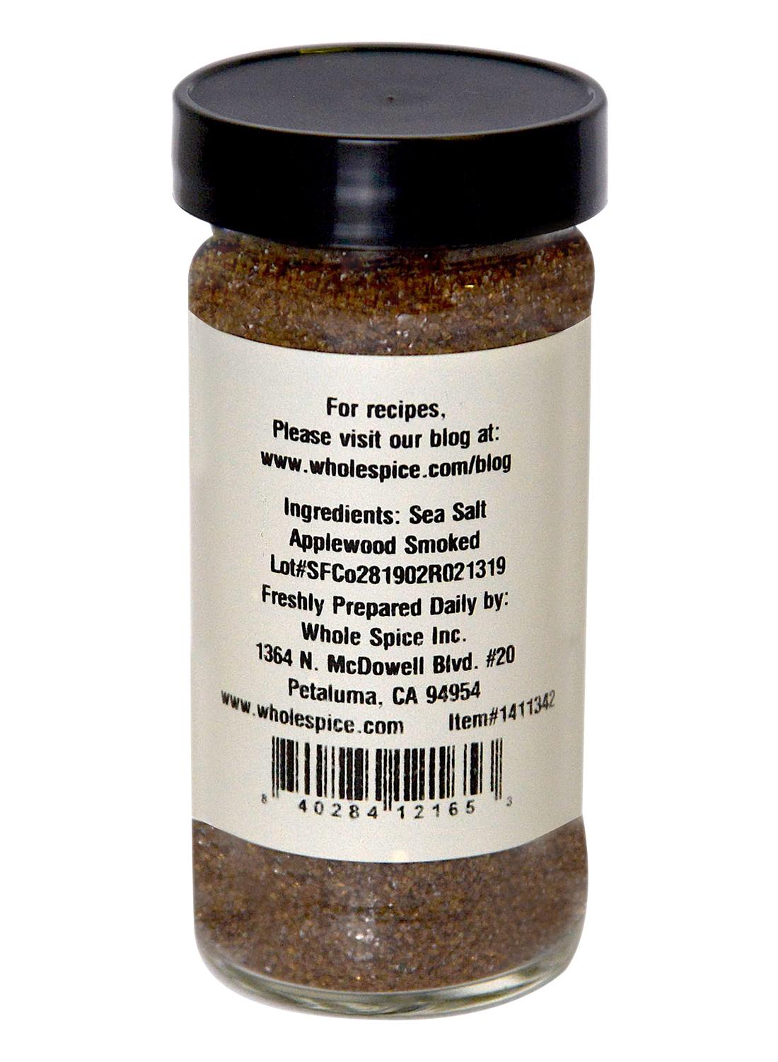 A glass jar of Applewood Smoked Sea Salt by Whole Spice Inc. features a black lid, label with natural sea salt and applewood smoked ingredients, contact info, barcode, and the company's website.