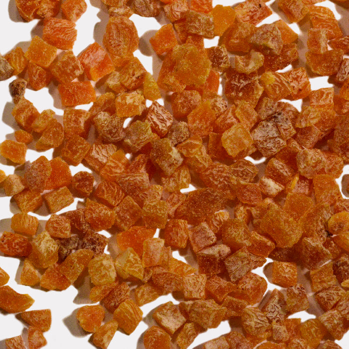 Whole Spice Inc. Apricot Dices—small, orange-brown cubes with a slightly rough, sugary surface—are scattered on a white background. Each piece varies in size and shape, making them a perfect healthy snack.