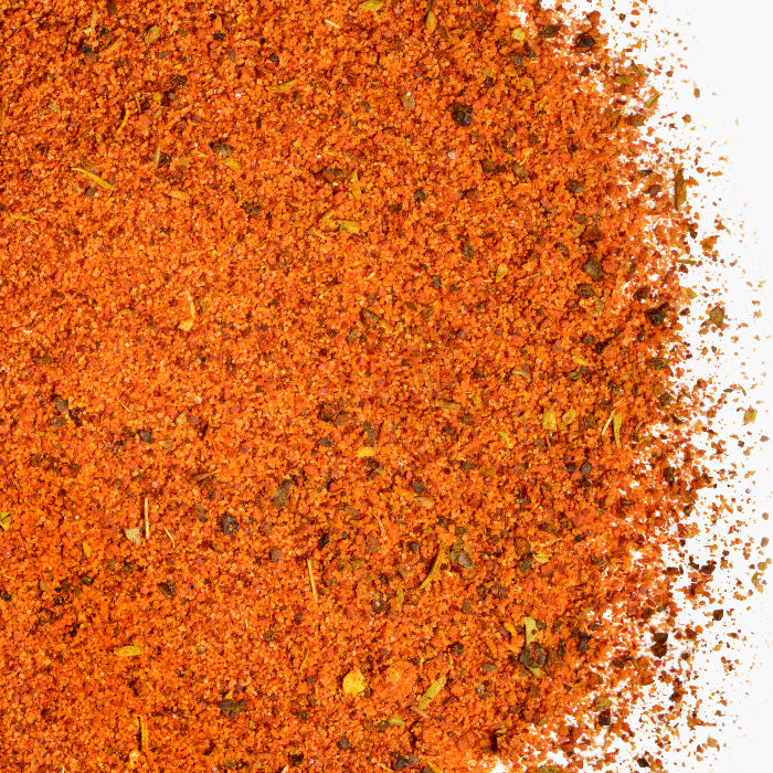A close-up of vibrant orange-red Asado Seasoning by Whole Spice Inc., showcasing fine texture and herb flecks—ideal for seasoning roasted chicken or classic pollo asado.