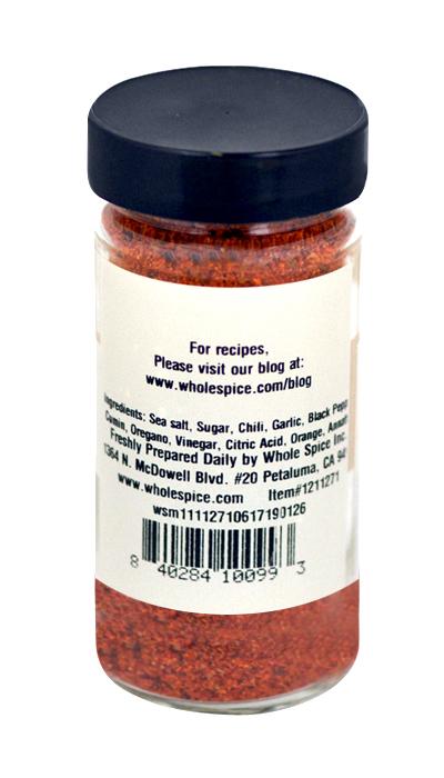 A clear spice jar with a black lid from Whole Spice Inc. holds vibrant red-orange Asado Seasoning for roasted chicken, featuring a label with ingredients and barcode.