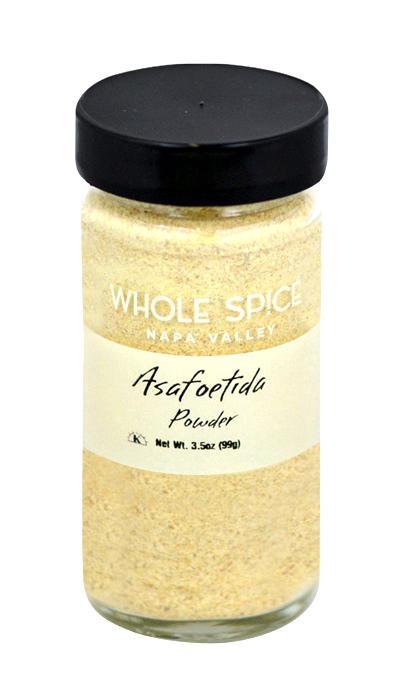 A clear glass jar with a black lid holds Whole Spice Inc. Asafoetida Powder, a popular Indian flavor enhancer. The label states: Asafoetida Powder, Net Wt. 3.5oz (99g).