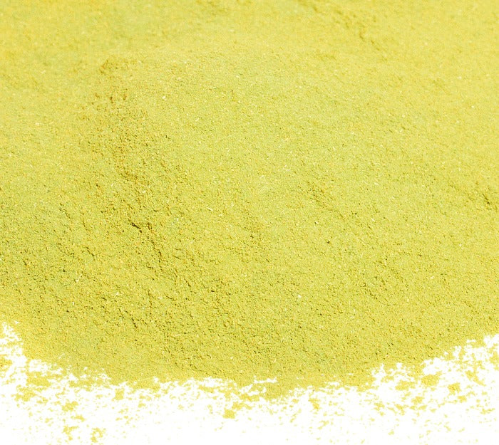 A close-up of Whole Spice Inc.'s Bay Leaves Ground Organic—a fine, light yellow-green powder—spread across a white surface.