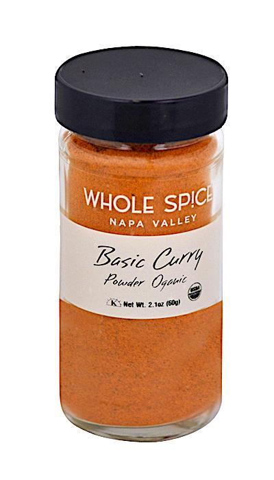 A clear glass jar with a black lid by Whole Spice Inc., labeled Basic Curry Powder Organic, contains bright orange organic spices ideal for Indian dishes. Net weight: 2.1 oz (60g).