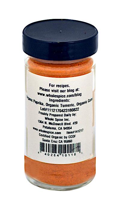 A small clear jar with a black lid contains orange Basic Curry Powder Organic by Whole Spice Inc. The label lists organic spices for Indian cooking—paprika, turmeric, cumin—and includes barcode, address, and website.