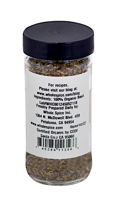 A clear spice jar with a black lid contains Whole Spice Inc. Basil Organic—dried sweet basil leaves, 100% organic and CCOF certified. The label lists ingredients, company contact info, and a barcode.