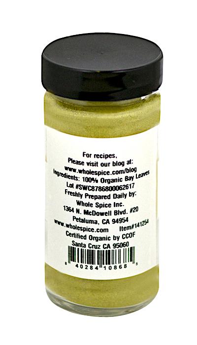 A glass jar with a black lid contains Bay Leaves Ground Organic by Whole Spice Inc.—100% organic laurus nobilis powder. The label includes ingredients, company details, location, and a website for recipes.
