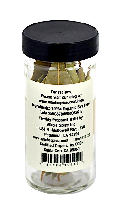 A clear glass jar with a black lid contains Bay Leaves Whole Organic by Whole Spice Inc. The label states 100% organic bay leaf, with company and certification details on the back.