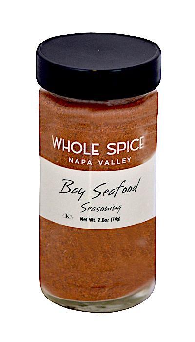 A clear glass jar with a black lid labeled Whole Spice Inc. Bay Seafood Seasoning holds 2.6 oz (74g) of reddish-brown all-purpose seafood seasoning blend.