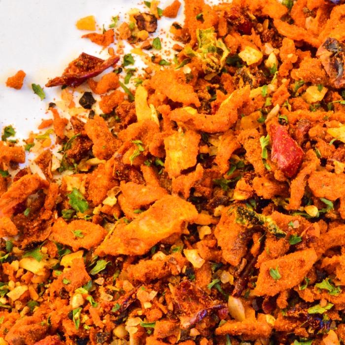 Close-up of Whole Spice Inc. Beans Seasoning, a colorful blend with dried red chilies, crispy onions, green herbs, and seasoning flakes—perfect for adding flavor to beans.