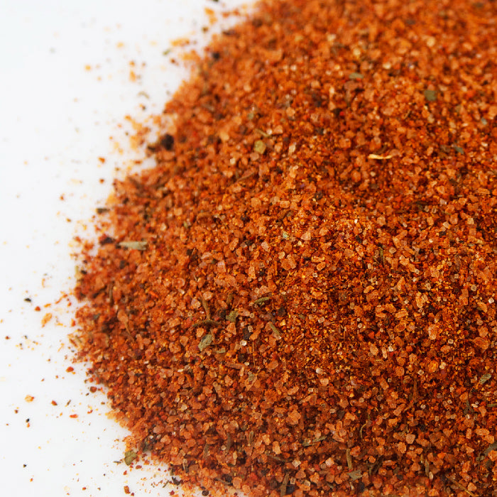 A close-up of Whole Spice Inc. Beef Rub, a reddish-brown grilling seasoning with visible herbs and spices, displayed on a white surface.