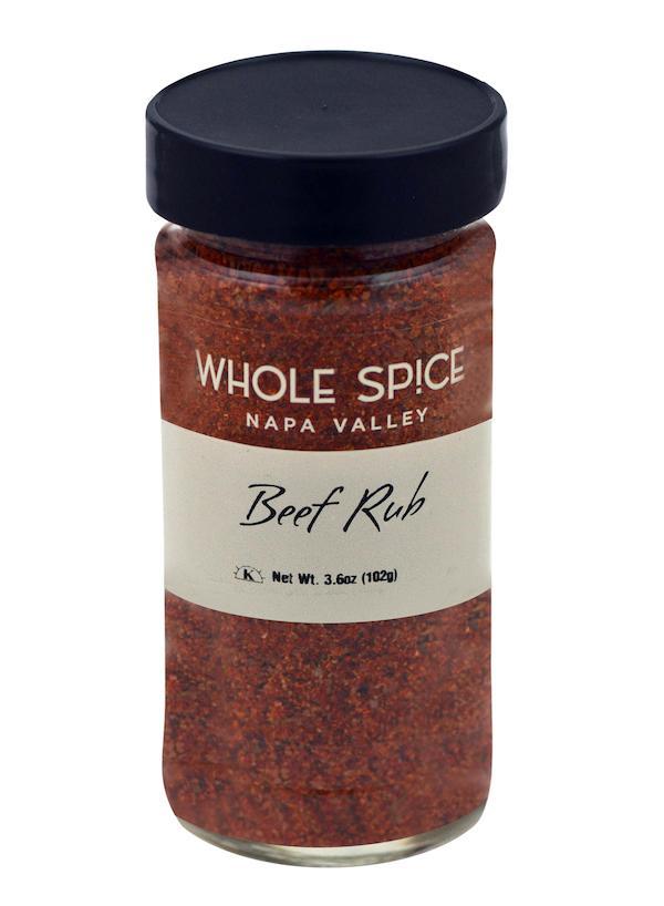 A clear glass jar with a black lid, labeled Whole Spice Inc. Beef Rub, contains a reddish-brown steak rub ideal for marinades or grilling. The net weight shown is 3.6 oz (102g).