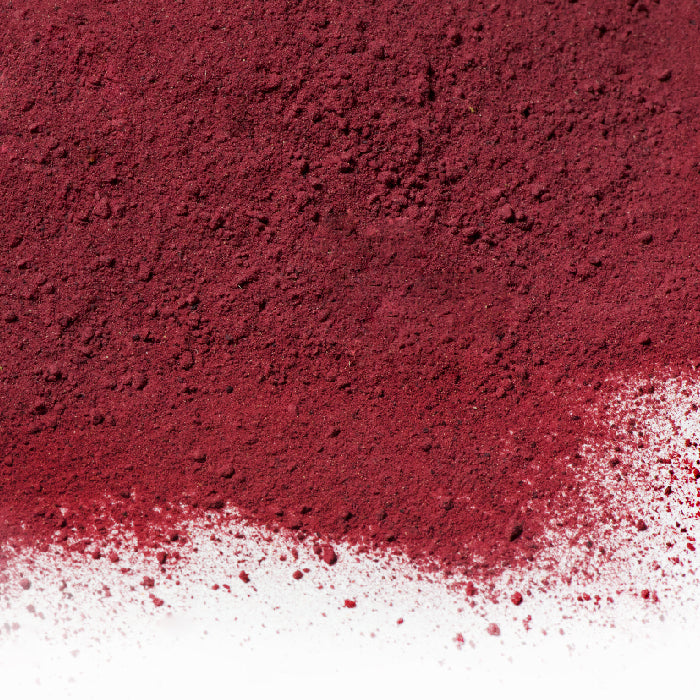 A close-up of Beet Powder by Whole Spice Inc., a natural colorant made from dehydrated ground beets, scattered on a white surface with a textured, grainy appearance.