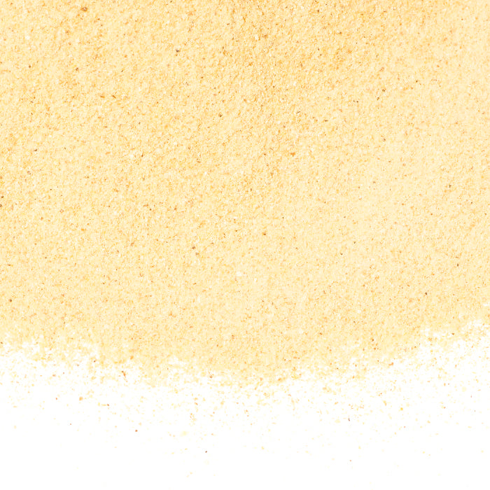 A close-up of Whole Spice Inc. Blood Orange Peel Powder—fine, light yellow, and evenly ground—scattered on a white surface with some loose granules, making it ideal for baking.