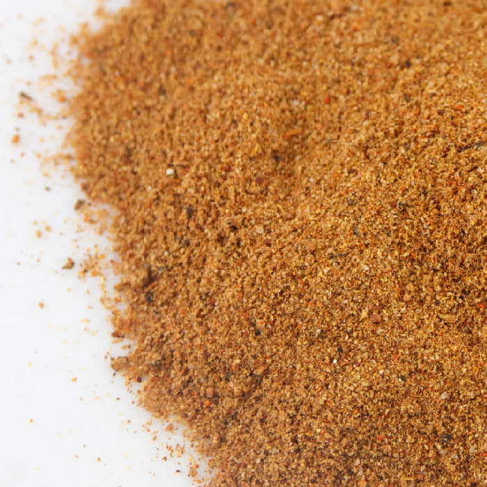 A close-up of Whole Spice Inc.'s Bloody Mary Mix—a fine, brown spice blend with visible herb and spice flecks on a white surface—perfect for adding bold flavor to your next cocktail.