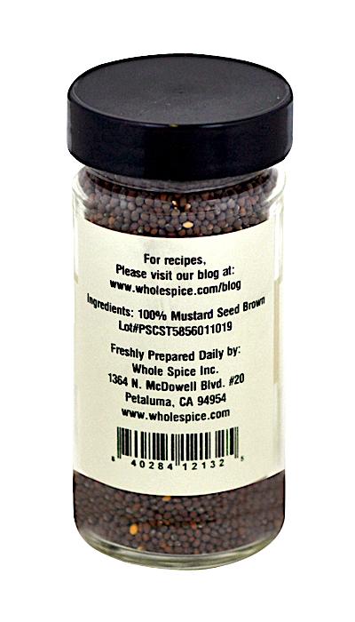 A clear glass jar with a black lid from Whole Spice Inc. contains Brown Mustard Seed Whole (100% Brassica nigra). The label lists ingredients, supplier details, and includes a barcode.