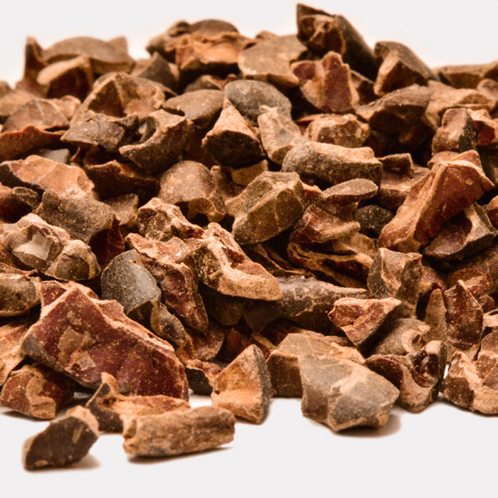 A close-up image of Whole Spice Inc. Cacao Nibs shows their rough texture and dark brown color. These crunchy pieces from roasted cocoa beans deliver an intense flavor—ideal for chocolate lovers—against a white background.