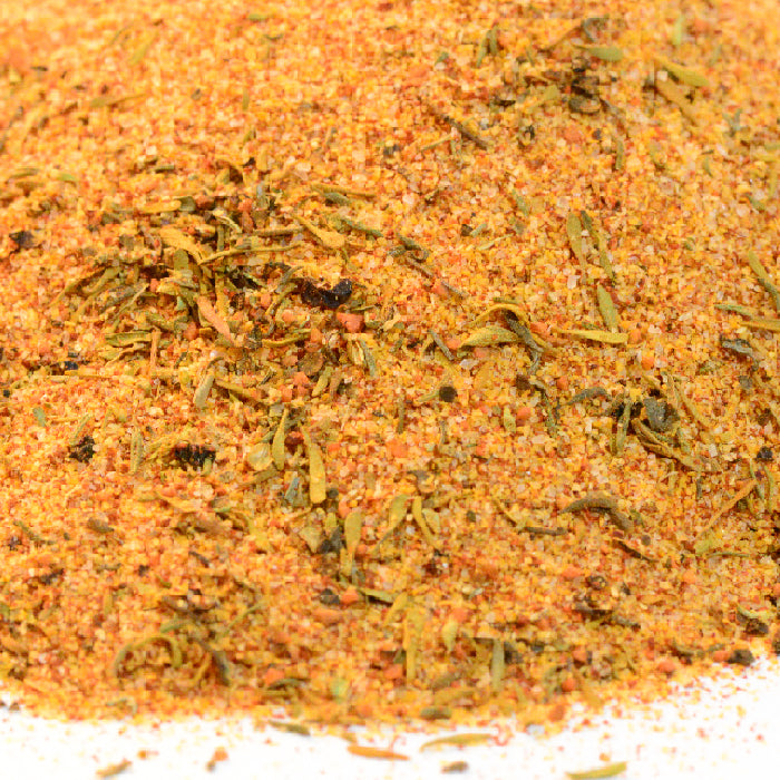 A close-up of Whole Spice Inc. Cajun Seasoning displays its colorful, textured blend with visible green and orange flecks of dried herbs and spices on a white surface.